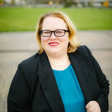 A blond woman in blue shirt and black blazer.